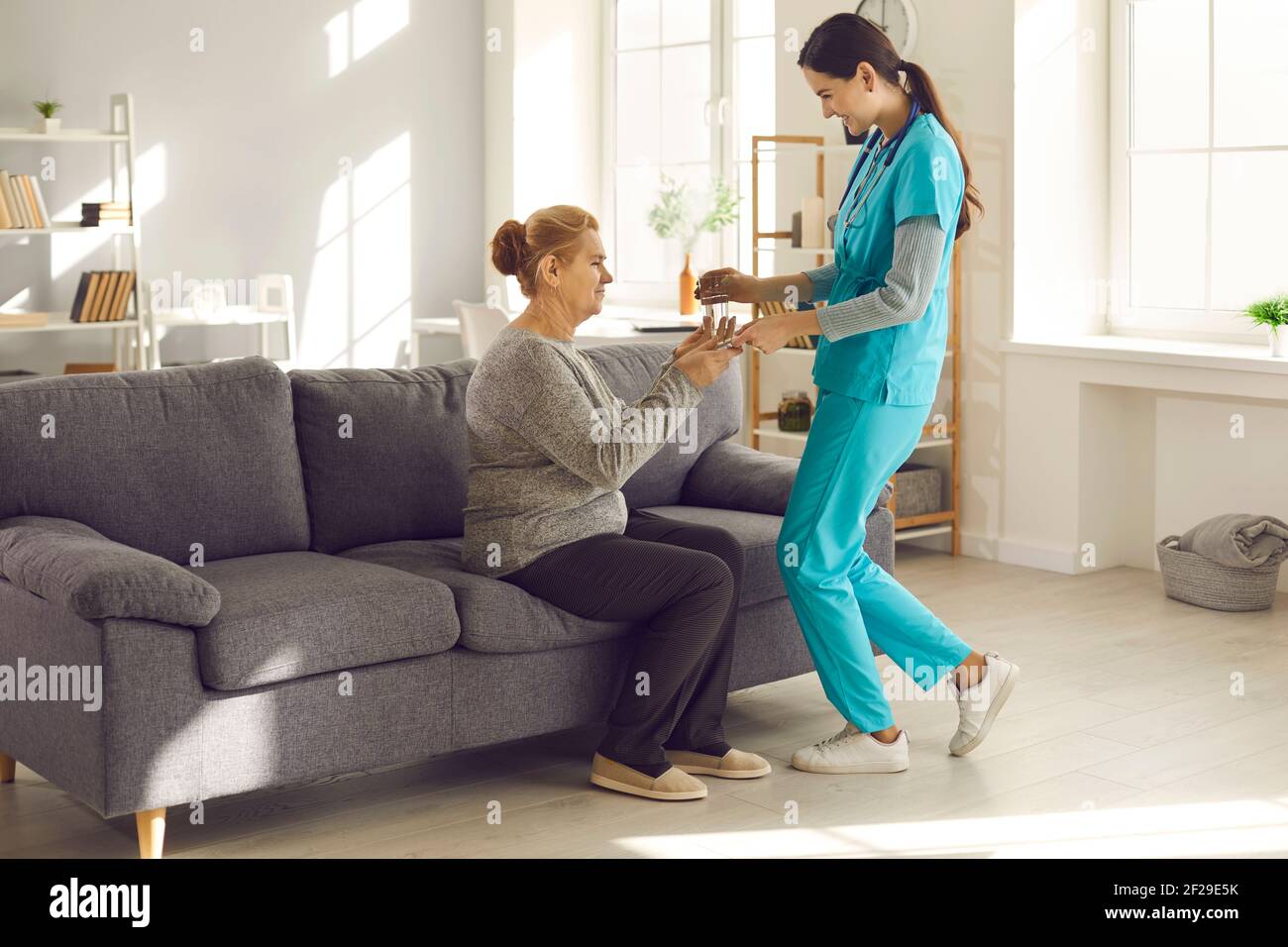 Friendly nurse at hospital or assisted living facility giving glass of water to mature woman Stock Photo