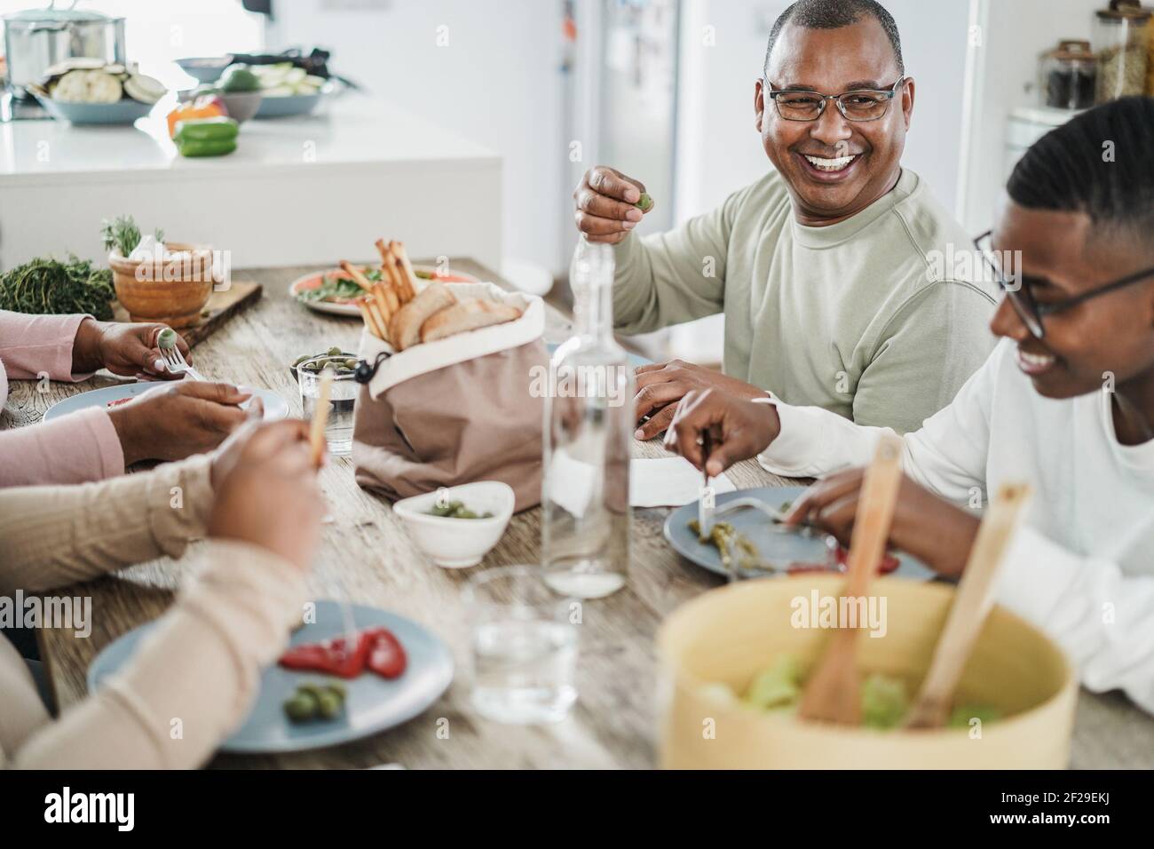 Happy black family eating lunch at home - Father, daughter, son and mother having fun together sitting at dinner table - Main focus on man face Stock Photo