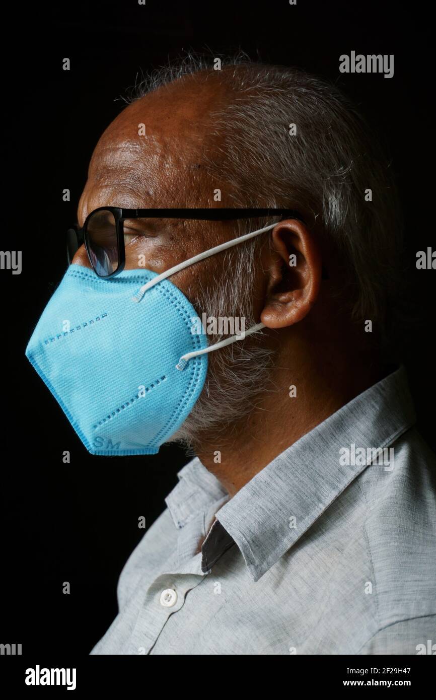 Portrait of 60 years old Indian man wearing a blue mask, isolated on a black background, in order to protect himself from COVID-19. Stock Photo