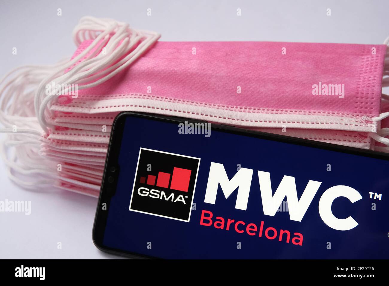Mobile World Congress Barcelona logo seen on the screen of smartphone and pile of face masks on the background. Concept for event during COVID pandemi Stock Photo