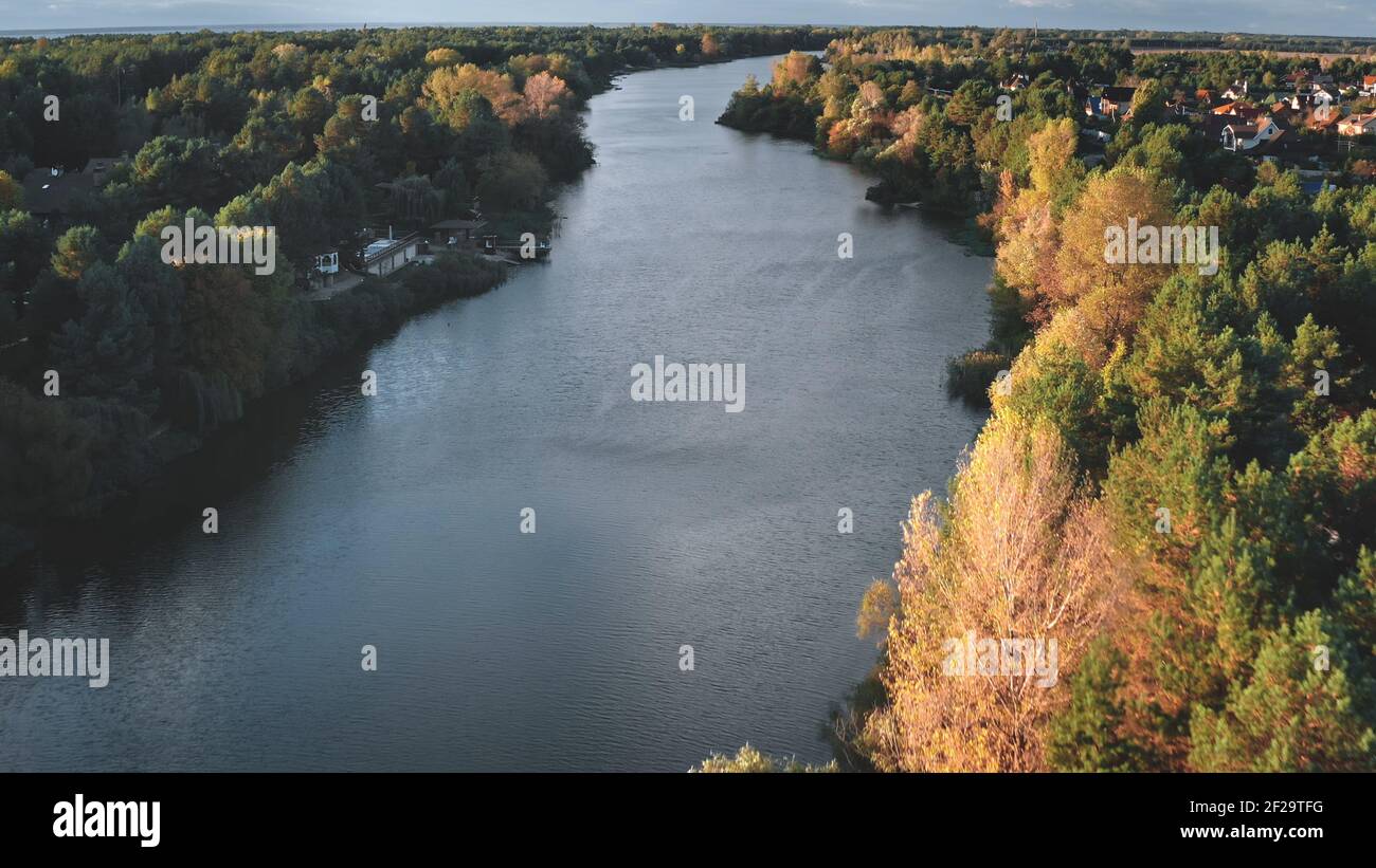 Cityscape at river shore aerial. Autumn nobody nature landscape. Colorful leafy trees forest at sun day. Cottages at city streets. Urban buildings at downtown suburbs. Green grass valley stream shore Stock Photo