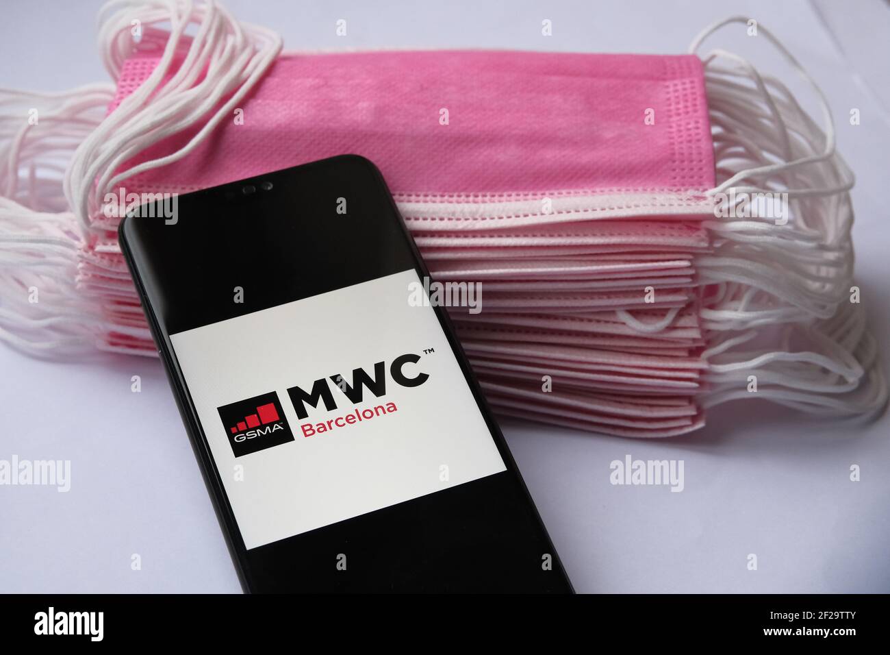 Mobile World Congress Barcelona logo seen on the screen of smartphone and pile of face masks on the background. Concept for event during COVID pandemi Stock Photo