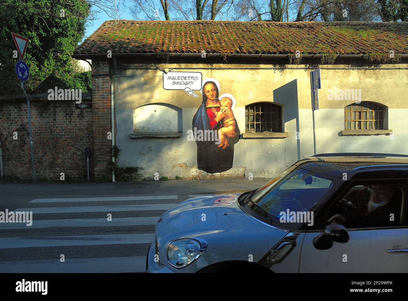 Padua, Italy. A mural of Mary, mother of Jesus against smog. Virgin Mary plugs with her fingers the nose of baby Jesus. Stock Photo