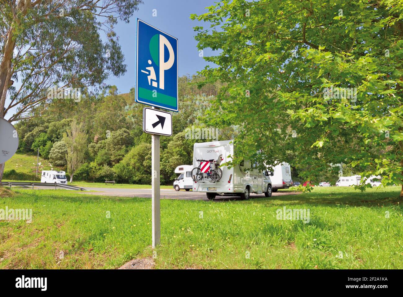 Camper vans parked at a parking at picknick place surrounded by green trees and grass with indication signal in the frontline Stock Photo