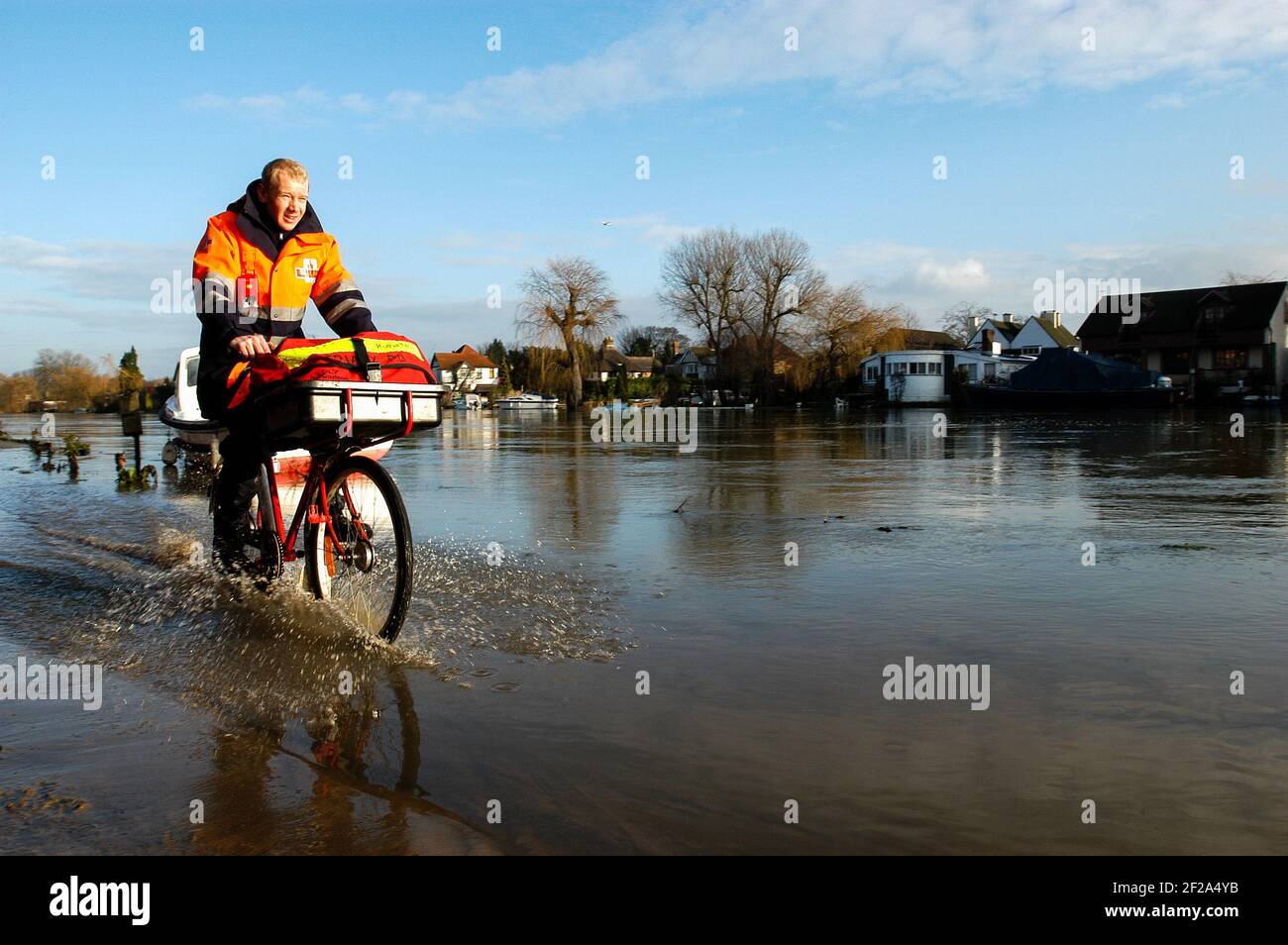 English postman cycling through a flood by the River Thames Stock Photo