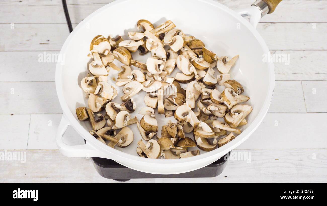 Sauteed organic baby bella mushrooms in a white frying pan Stock Photo