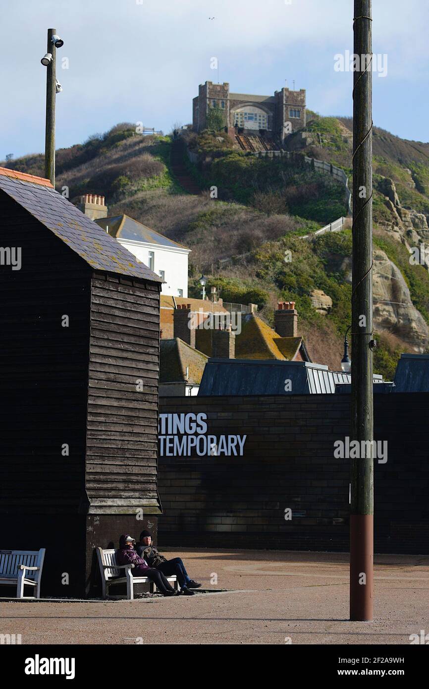 Hastings, East Sussex, UK. 11 Mar, 2021. UK Weather: The met office has issued a weather warning for high winds in the south. An elderly couple enjoy the sheltered bench from the wind in front of the famous net sheds. Photo Credit: Paul Lawrenson/Alamy Live News Stock Photo