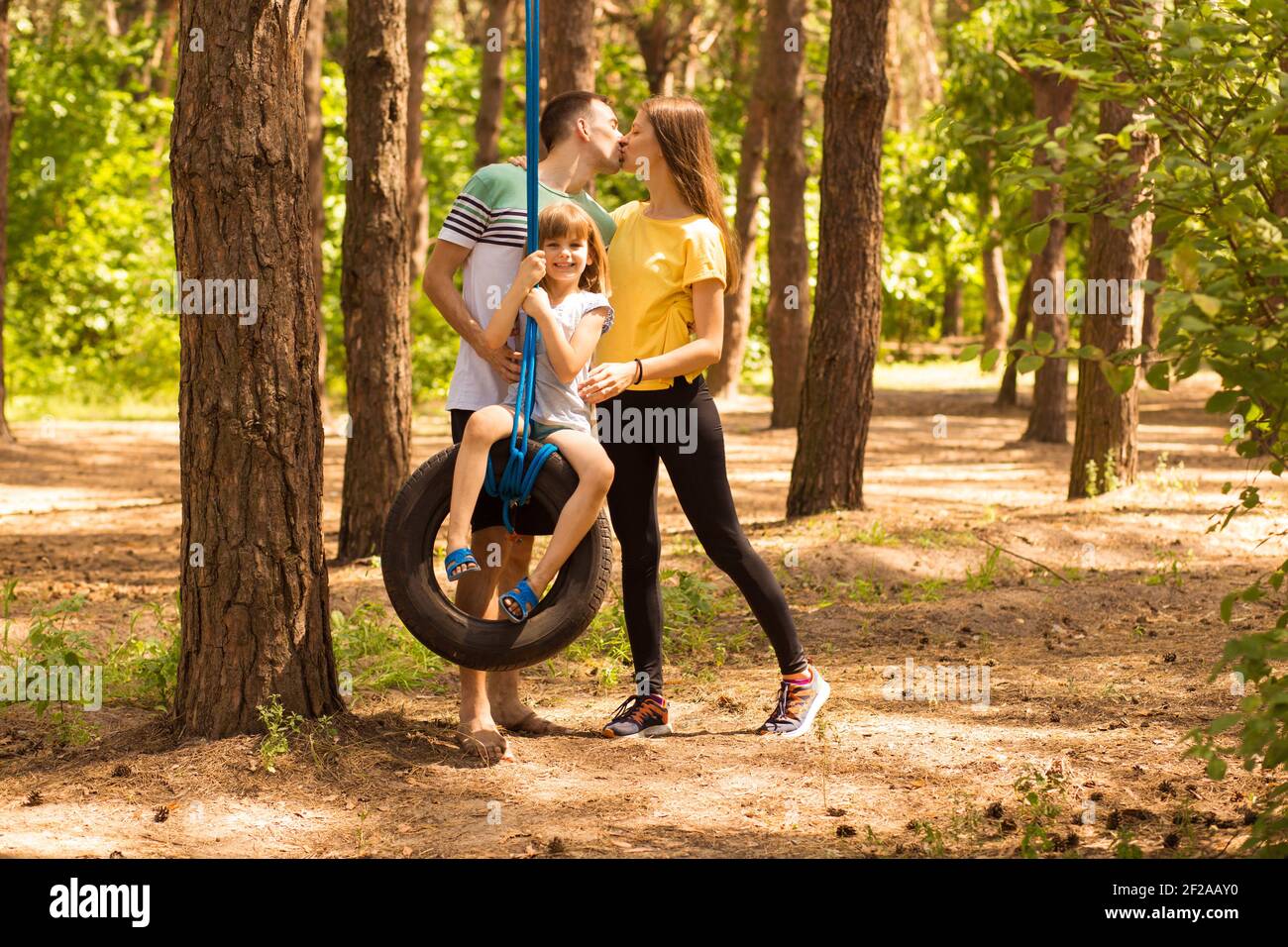 Lovely young happy parent which swing happy daughter on wheel, in summer nature on background, active time together Stock Photo