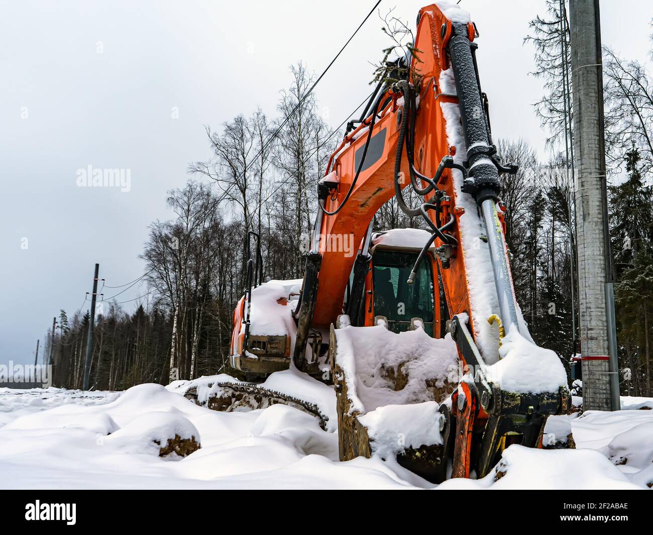 Large orange excavator covered with snow. Abandoned non-working broken construction equipment. Stock Photo