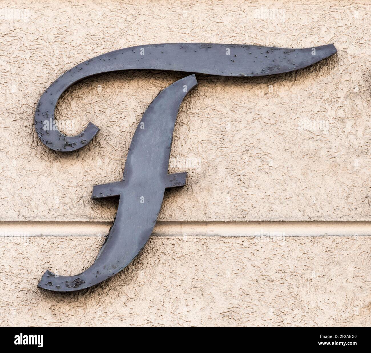 Grey metal letter F on a sand-coloured house wall Stock Photo