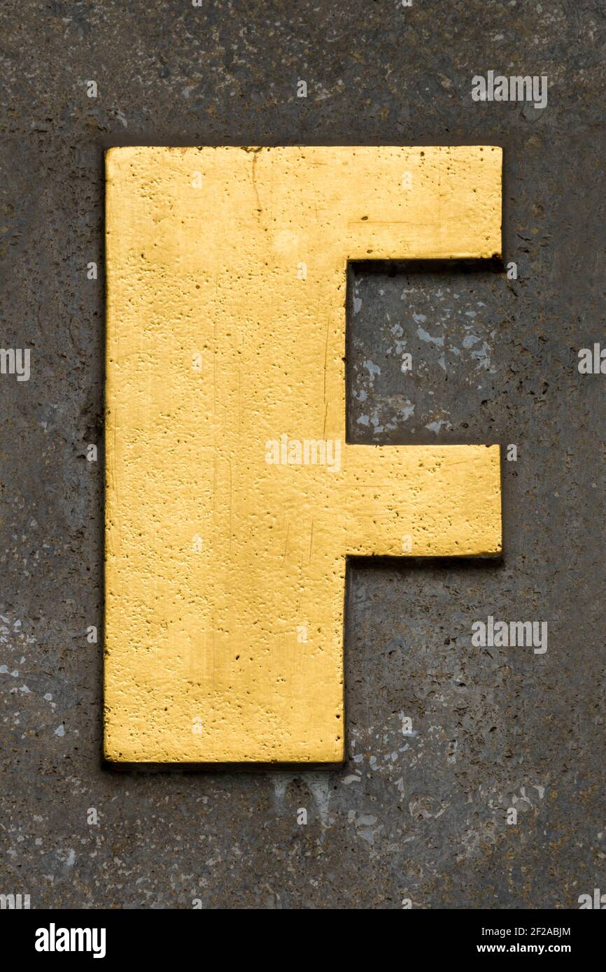 Golden letter F on a brown wall Stock Photo