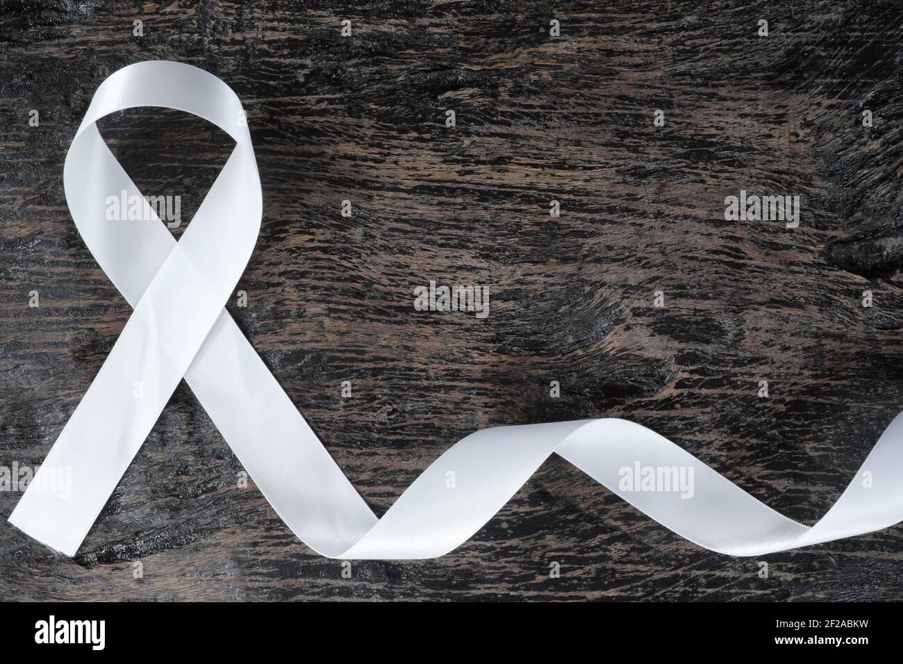 Top view of white ribbon on dark wood background. Lung cancer awareness