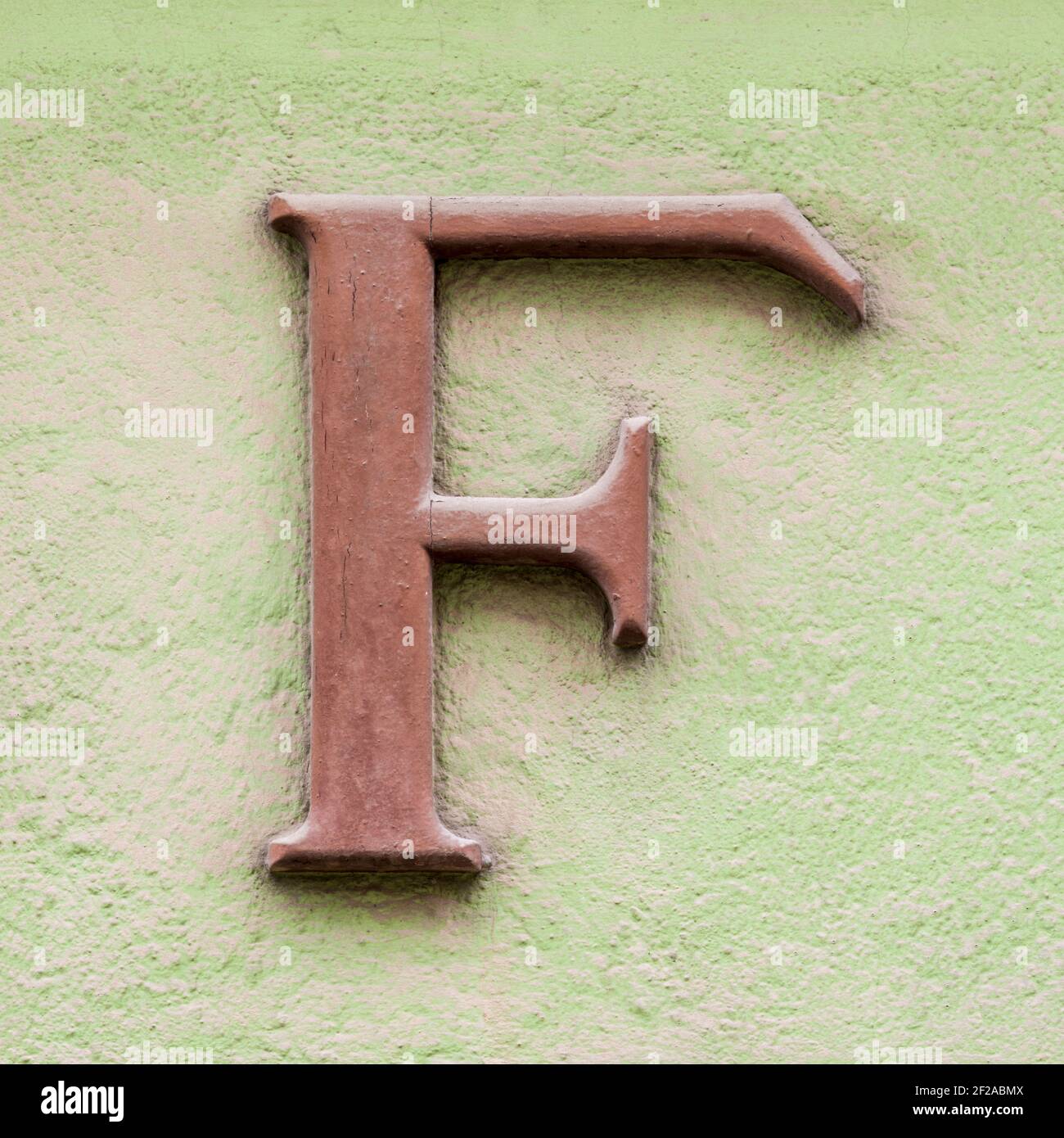 Brown letter F with serifs on green house wall Stock Photo