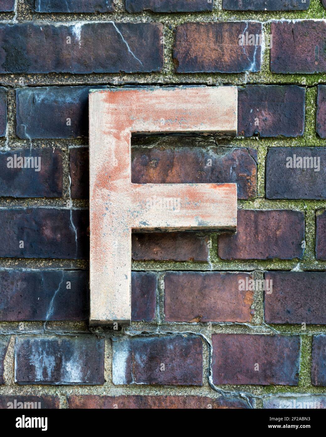 Weathered metal letter F in front of a brick wall Stock Photo