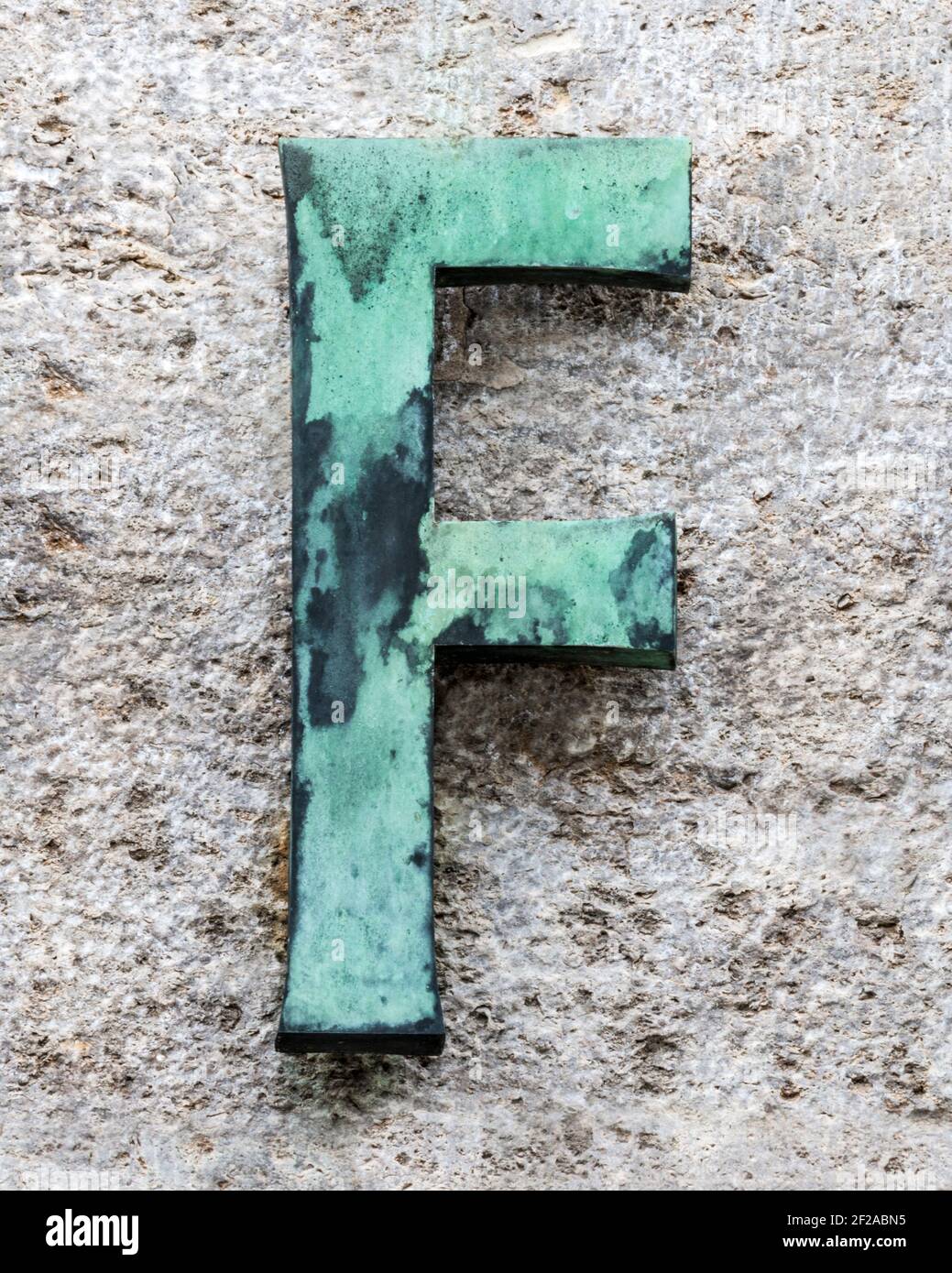 Metal letter F covered with verdigris on a natural stone wall Stock Photo