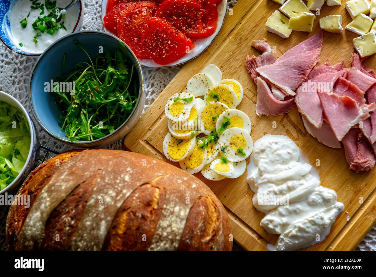 Continental, healthy breakfast containing homemade bread, vegetables tomatoes, argula, sald, cheese burratta, camembert, ham and egg. Stock Photo