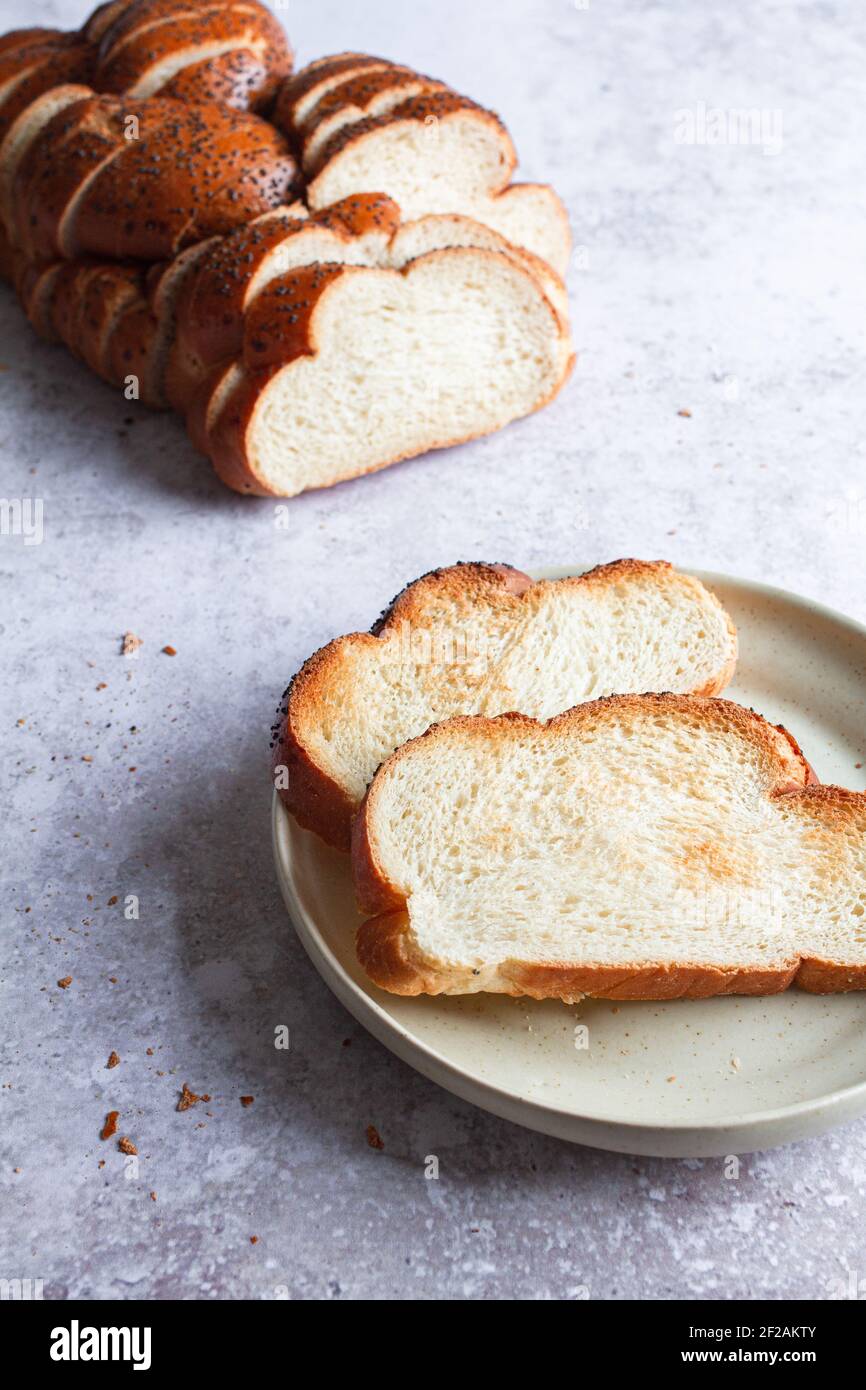Freshly sliced loaf of challah bread with two toasted slices on a plate. Stock Photo