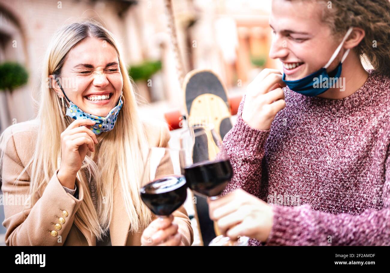 Young couple in love wearing open face masks and having fun at winery bar outdoors - Happy hipster lovers toasting wine at restaurant patio Stock Photo