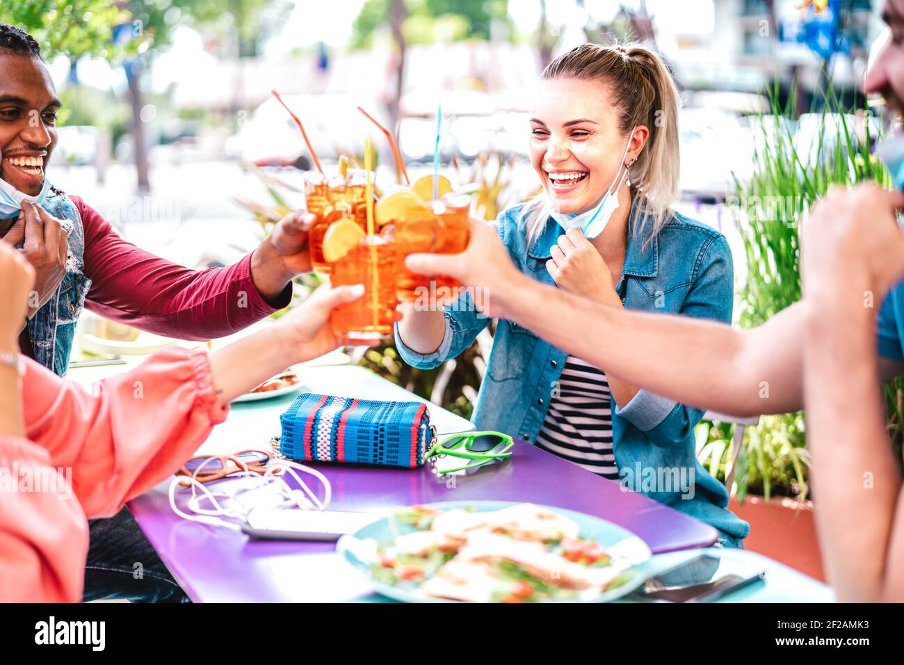 Young people drinking spritz at cocktail bar wearing face masks - New normal friendship concept with friends having fun together toasting drinks Stock Photo