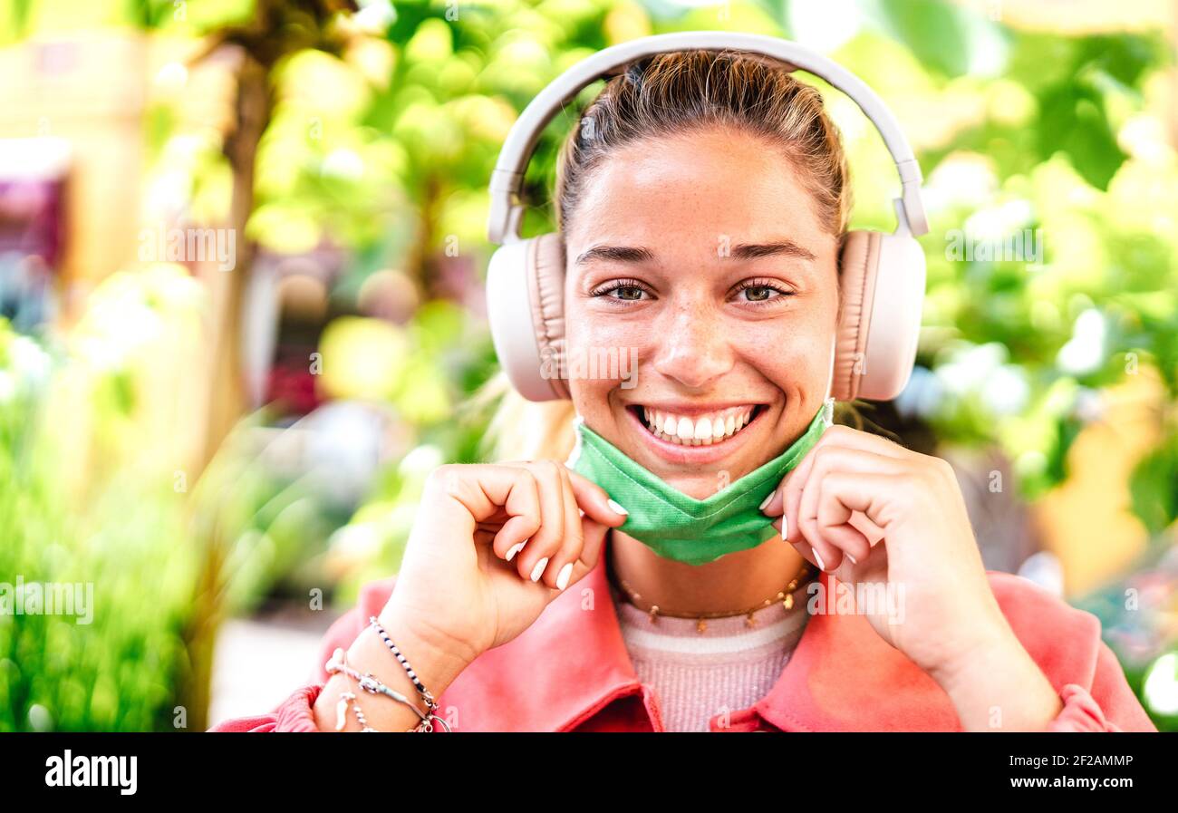 Young woman smiling looking at camera with open facial mask and headphones - New normal lifestyle concept with millenial girl having fun outdoors Stock Photo