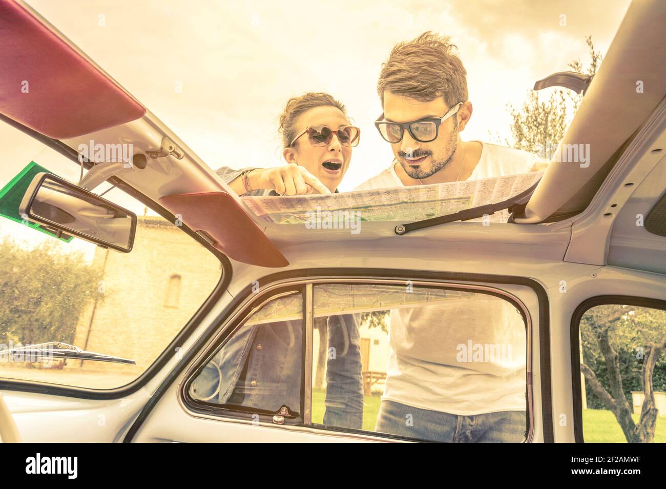 Couple of lovers looking at a map during honeymoon trip vacation - Vintage lifestyle traveling around the world with old retro classic car Stock Photo