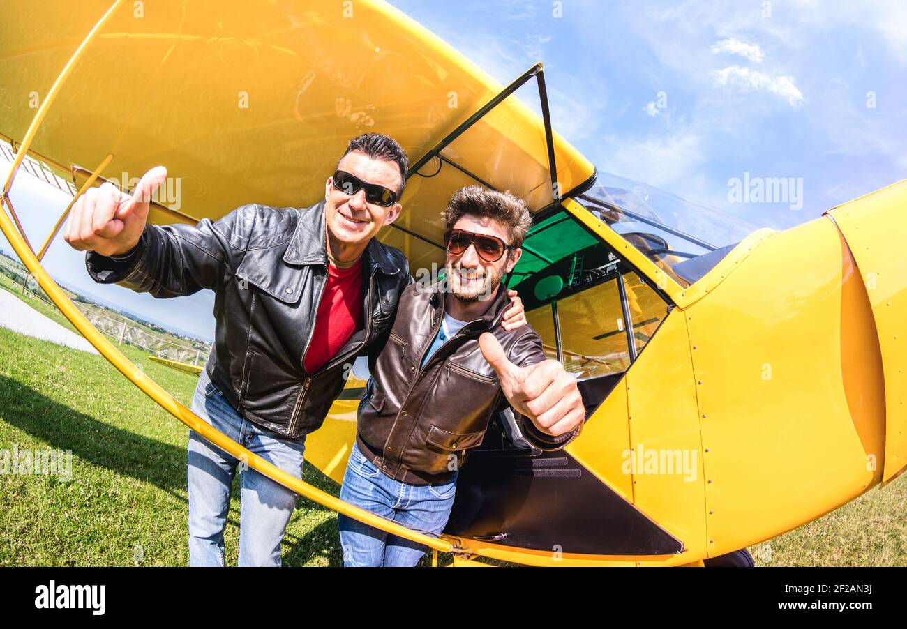 Happy best friends taking selfie at aeroclub with ultra light airplane - Luxury friendship concept about young people with thumbs up having Stock Photo
