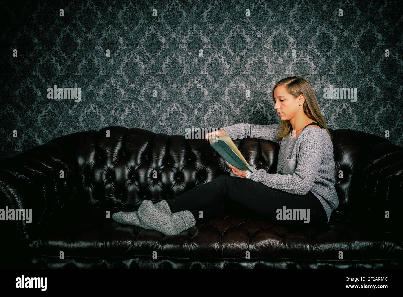 Student sits on sofa and learns from a book Stock Photo