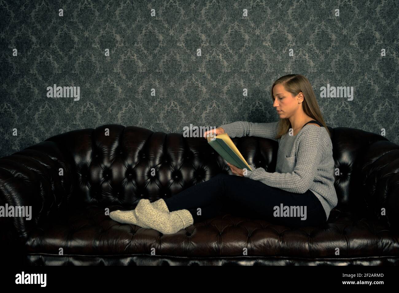 Girl in comfort clothing sitting relaxed on sofa and reading a book in book shop Stock Photo