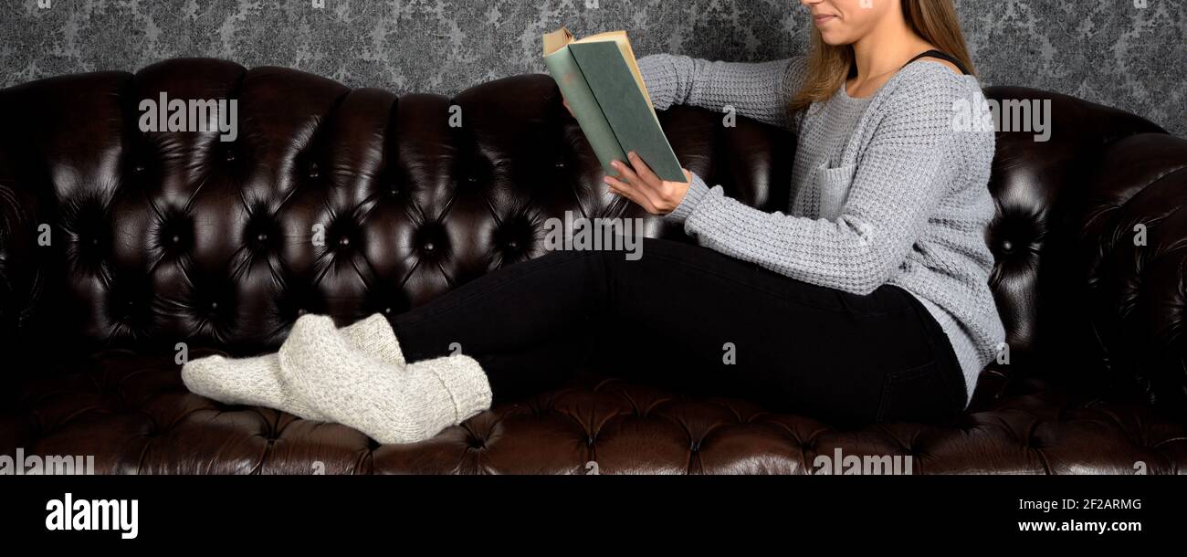 European female smiles and reads a book on her sofa Stock Photo