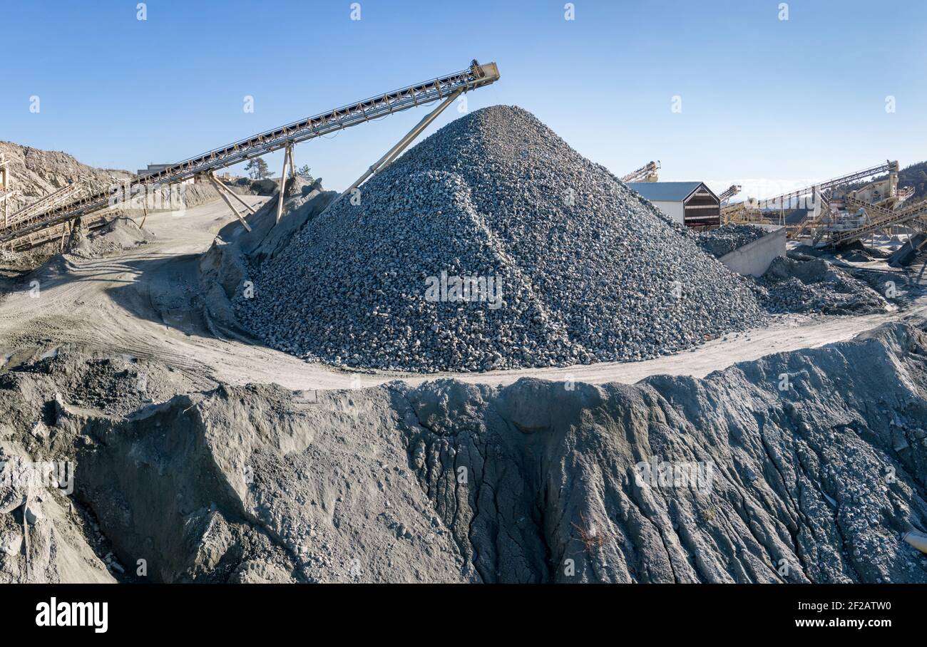 Huge pile of gravel and machinery at stone crushing and screening plant, over blue sky Stock Photo