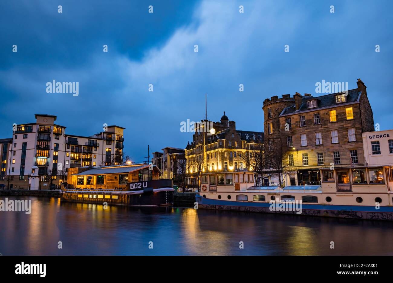 Barges, historic buildings, Malmaison Hotel & modern apartment block of flats lit up at night time, Water of Leith, The Shore, Edinburgh, Scotland, UK Stock Photo