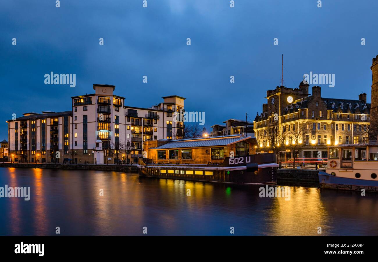 Barges, historic buildings, Malmaison Hotel & modern apartment block of flats lit up at night time, Water of Leith, The Shore, Edinburgh, Scotland, UK Stock Photo