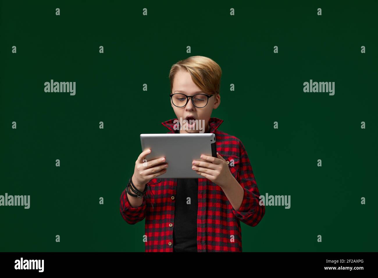 Surprised caucasian child boy in red checkered shirt using digital tablet on green background Stock Photo