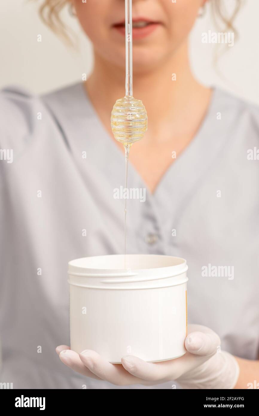 Beautician holding white bowl with wax flowing down from honey stick on a white background Stock Photo