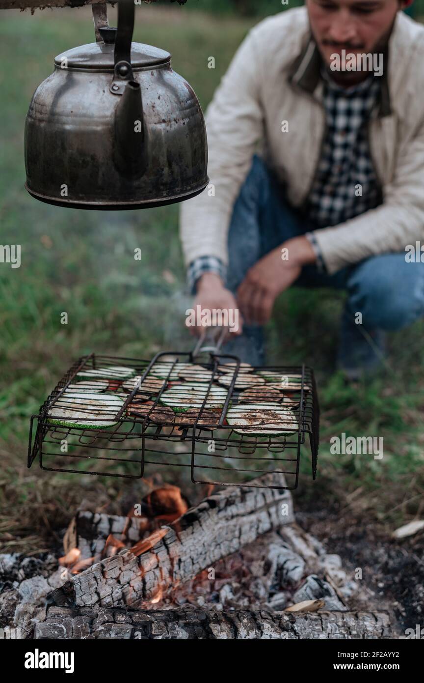 Young man fry vegetables on the grill on the fire. Stock Photo