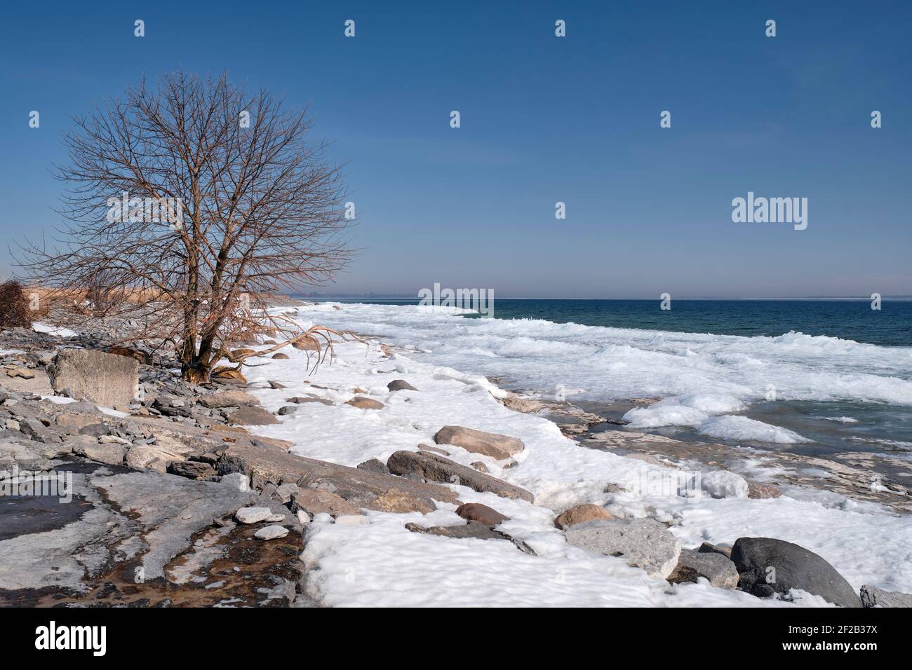 Ice piles up and snow starts to melt along the shore of Amherst Island in Lake Ontario, as winter comes to an end. Stock Photo