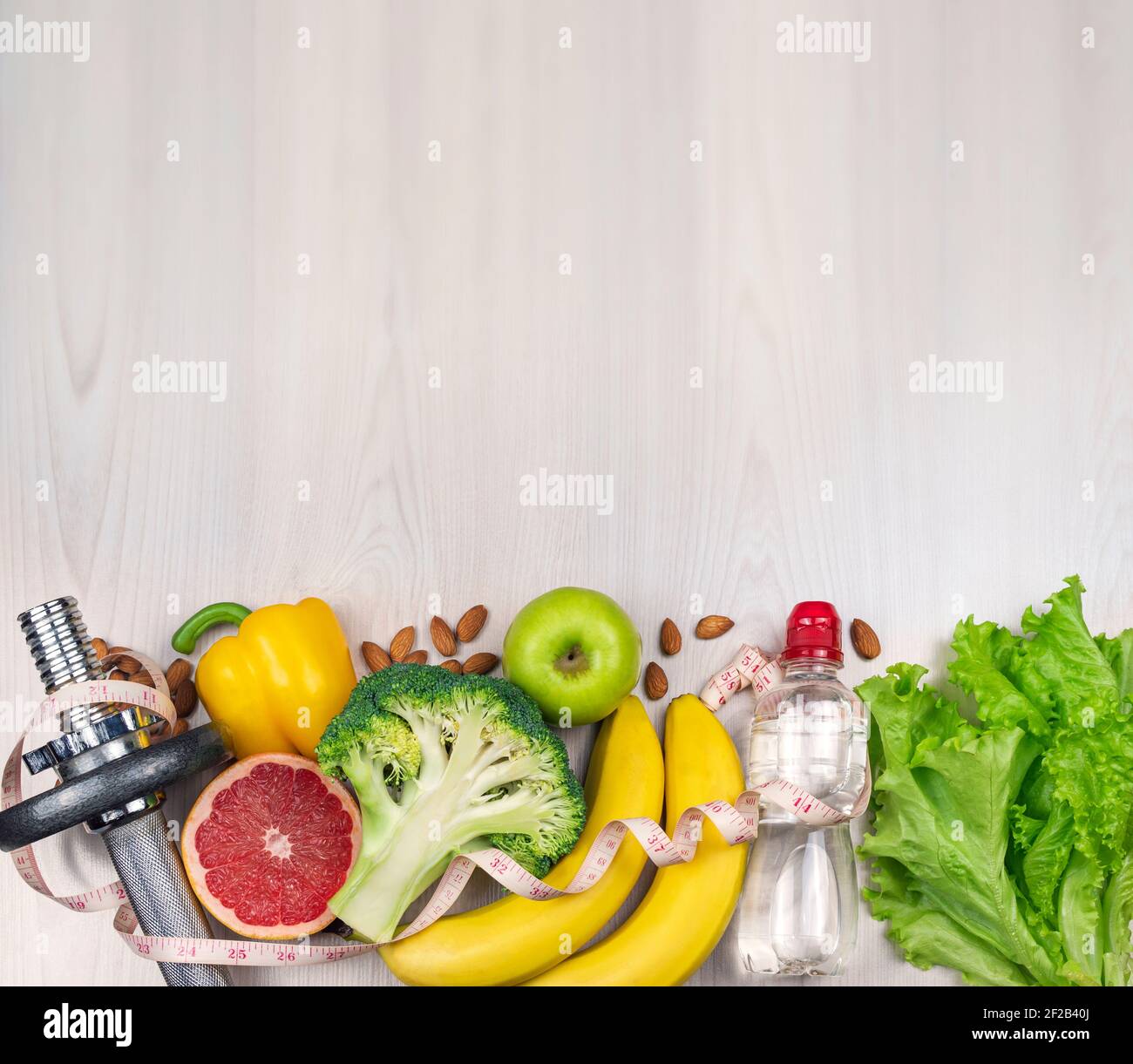 Fitness and healthy food lifestyle concept. Diet fruit and vegetable lunch box, dumbbell, water and measuring tape on bright background. Flat lay Stock Photo