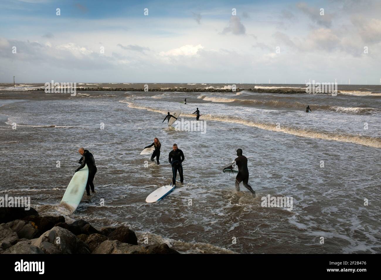 A group of surfers in the sea in the mouth of the river Mersey. High tides and a storm which swept across the United Kingdom brought favourable conditions for surfing in Leasowe Bay, Merseyside on 11 March, 2021. Stock Photo