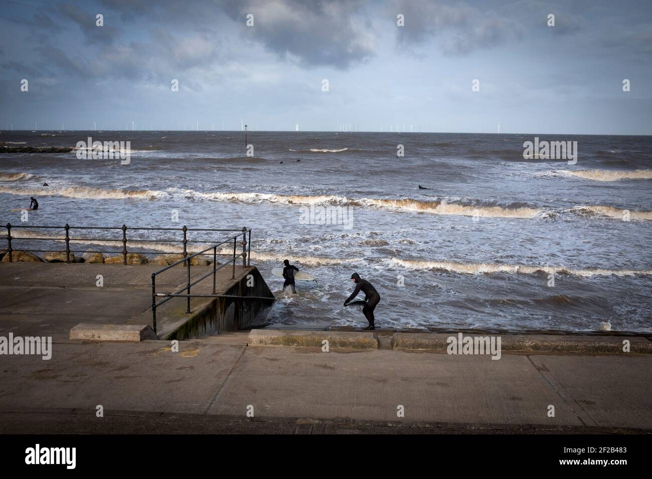 Two surfers walking towards the sea in the mouth of the river Mersey. High tides and a storm which swept across the United Kingdom brought favourable conditions for surfing in Leasowe Bay, Merseyside on 11 March, 2021. Stock Photo