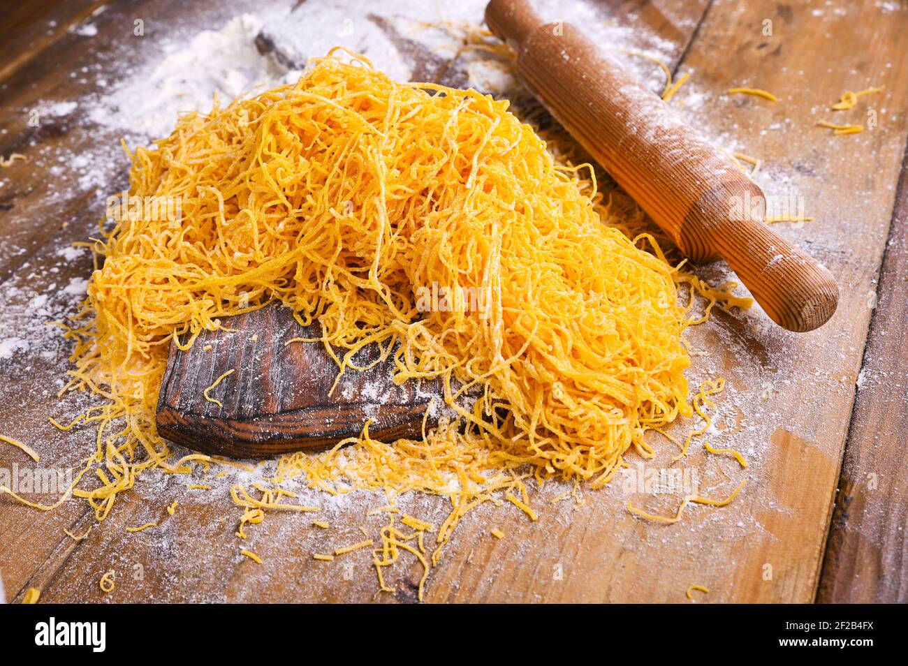 Tagliatelle pasta . Traditional Italian named Angel Hair (capellini d'angels). Woman cooking Italian egg pasta, homemade and fresh in flour on a cutting table.  Stock Photo