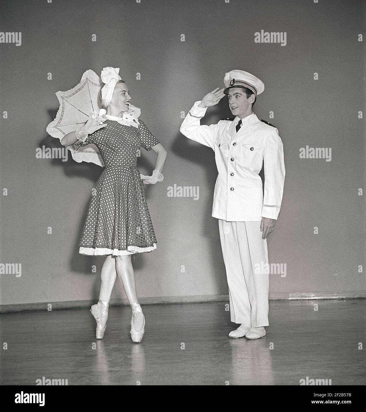 In the theatre in the 1940s. A ballet dancer on her toes in a dress and umbrella is greeted by a girl dressed in a white navy uniform who salutes her. Two members of a theatre ensemble. Sweden 1947. ref AC58-4 Stock Photo