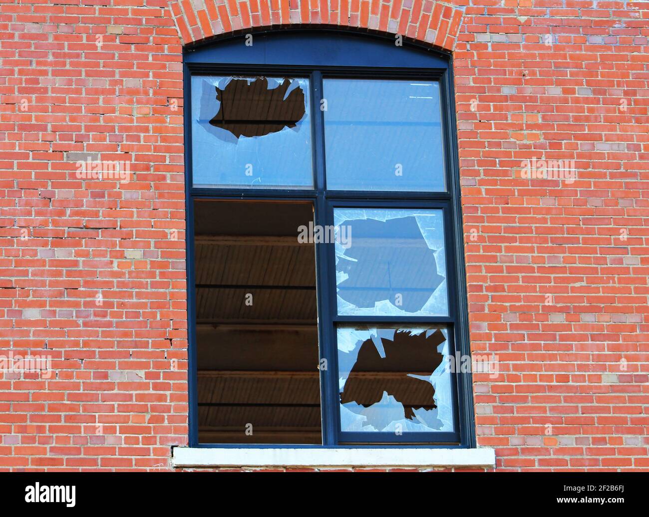 Close-up of a window, in a brick wall, in which all but one pane of glass has been broken. Stock Photo