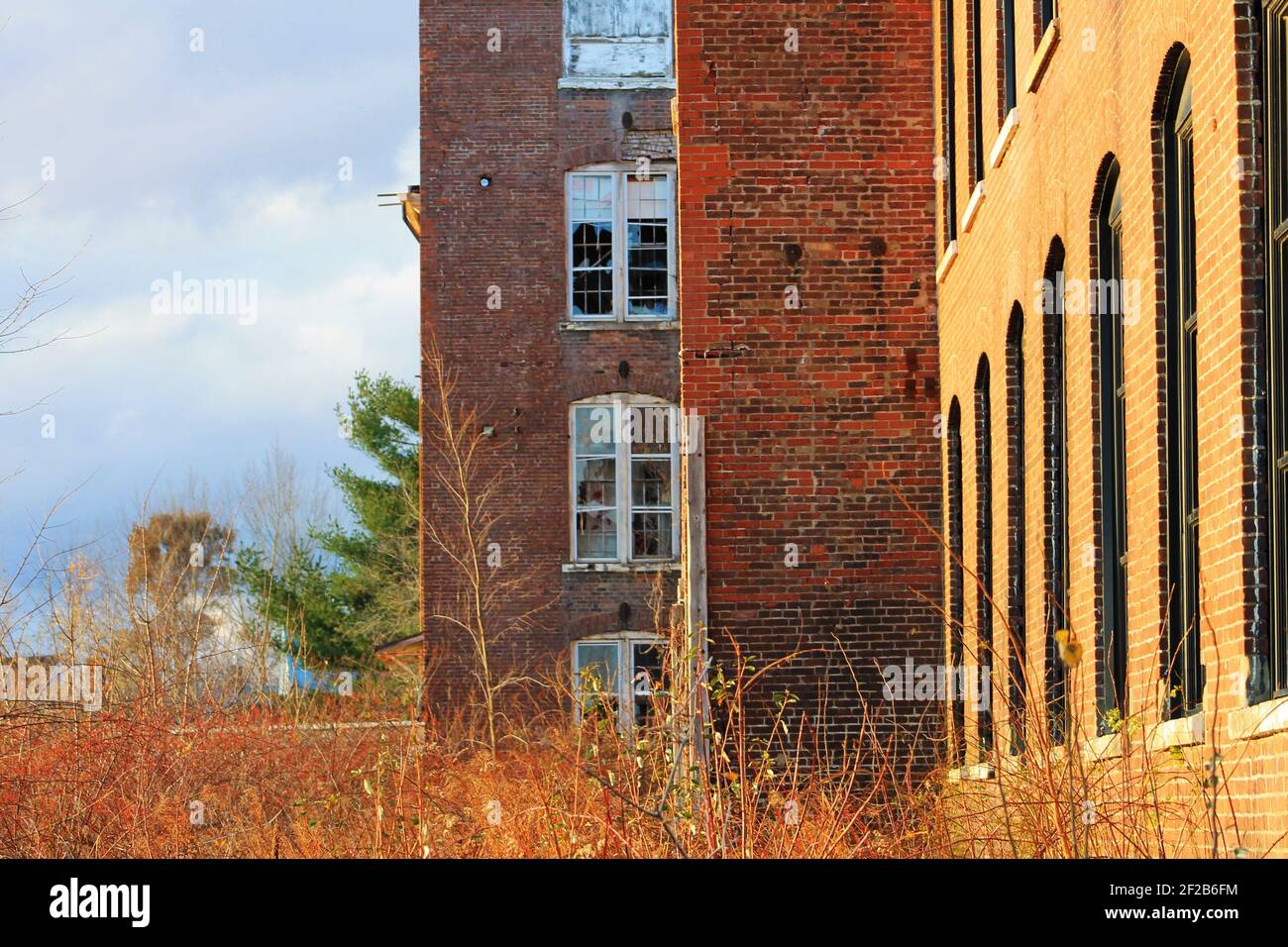 An old, abandoned, brick building that is falling into ruin, with broken windows and overgrown yard. Stock Photo