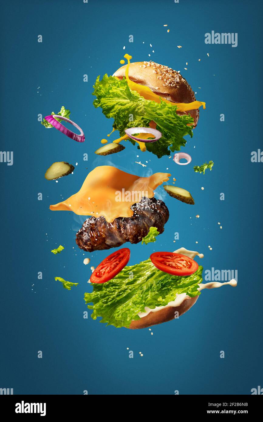 Hamburger with flying ingredients on blue studio background. Fast food concept. Bun, salad, meat, cheese and tomatos, onion in flight. Restaurant cuisine, advertising concept. Tasty, juicy, cheesy. Stock Photo