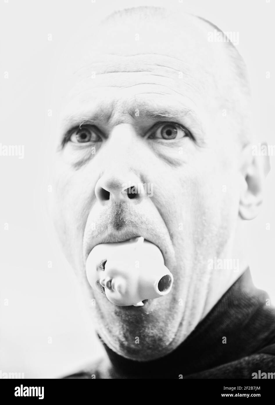 Black and white image of mid adult man holding dolls head in his mouth and shocked facial expression. Concept of shock, surprise, fright Stock Photo