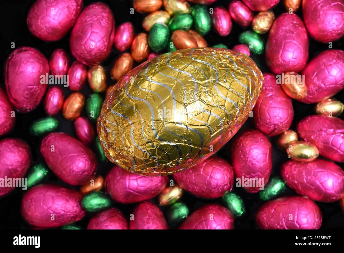 Pile or group of multi colored and different sizes of colourful foil wrapped chocolate easter eggs in pink, red, gold and lime green. Stock Photo