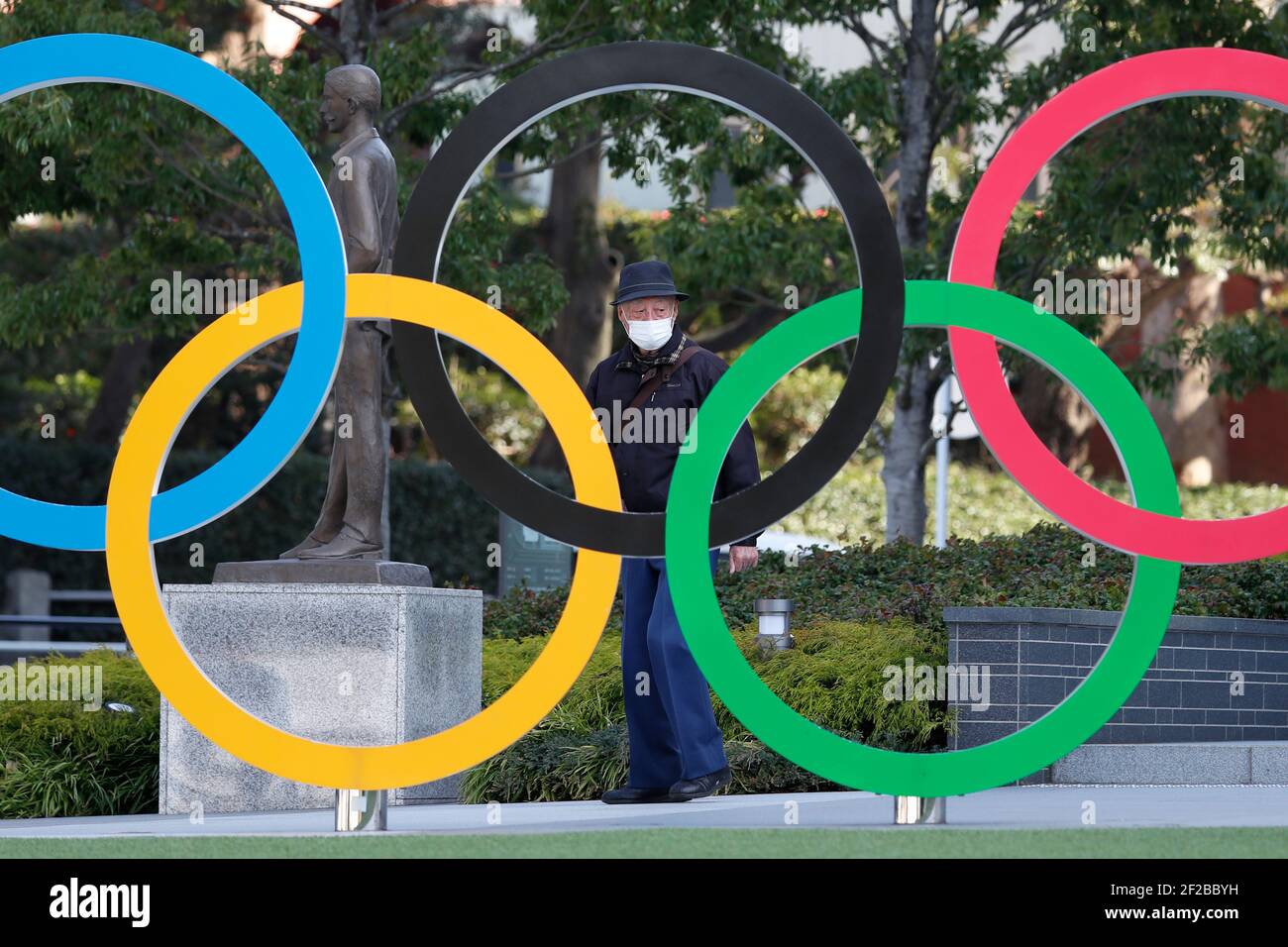 a-man-wearing-a-facemask-is-seen-behind-the-olympic-symbols-of-the-five