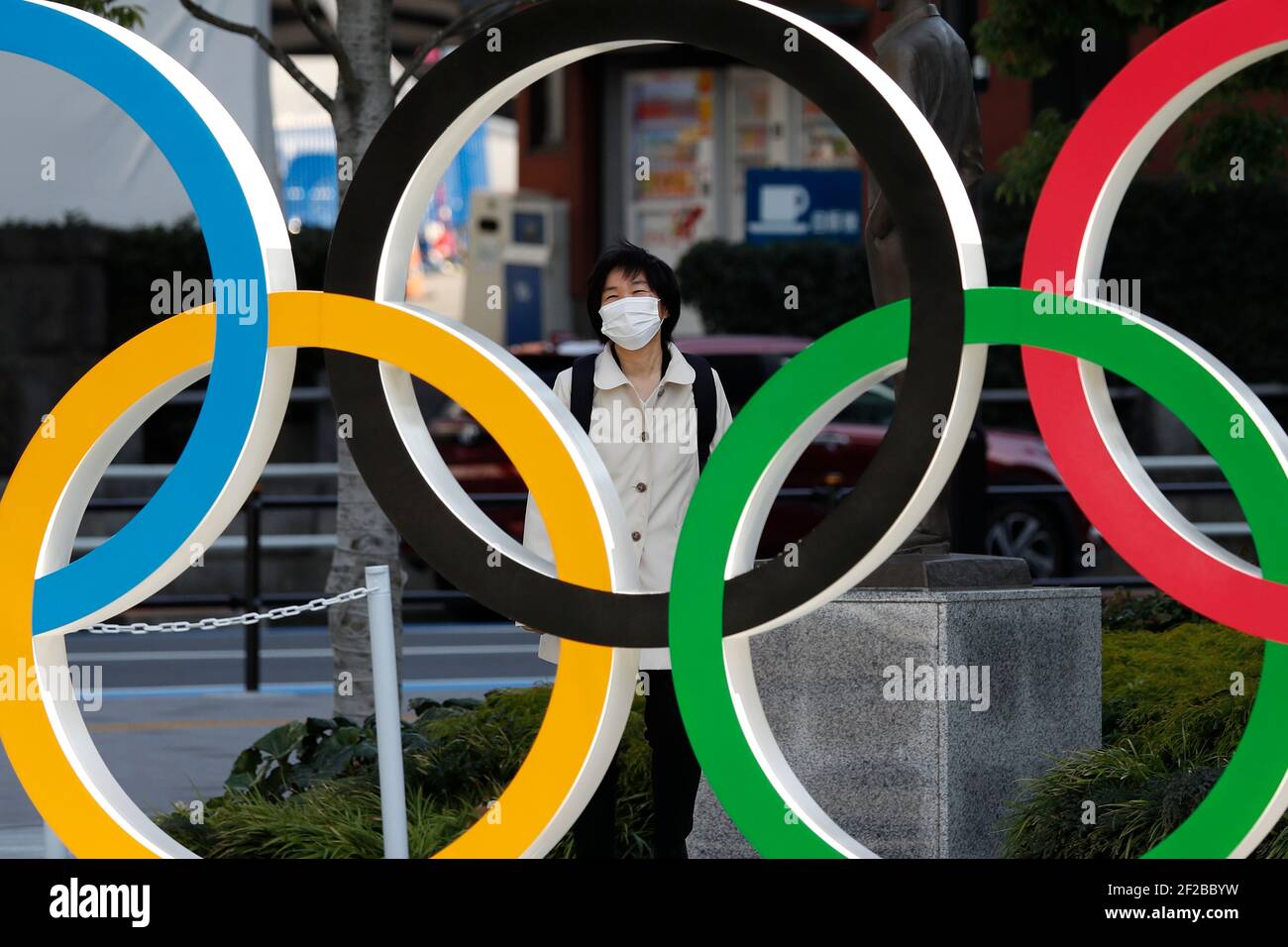 a-man-wearing-a-facemask-is-seen-behind-the-olympic-symbols-of-the-five