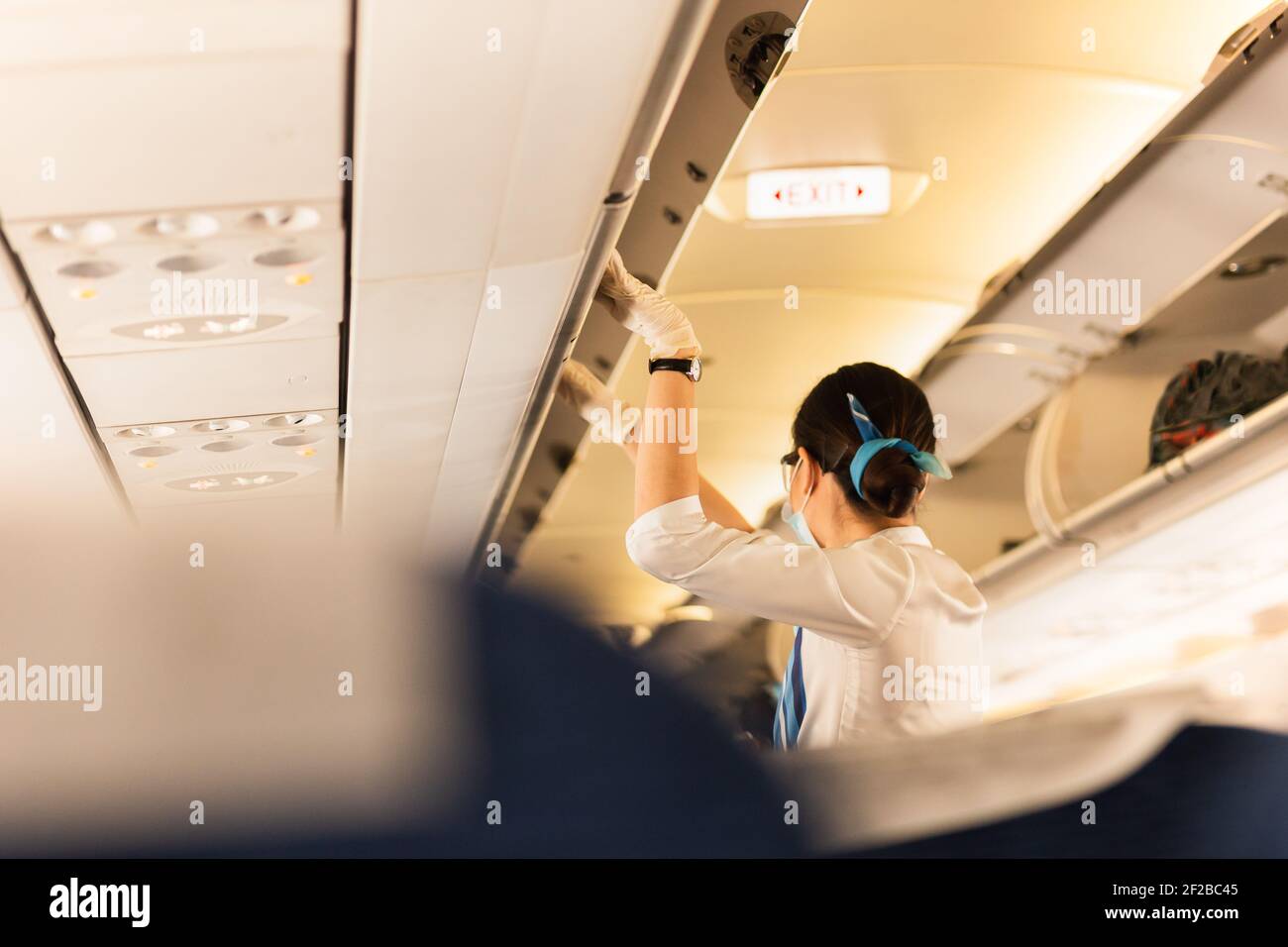 Flight attendant in protective masks and glove closing overhead compartment. Stock Photo