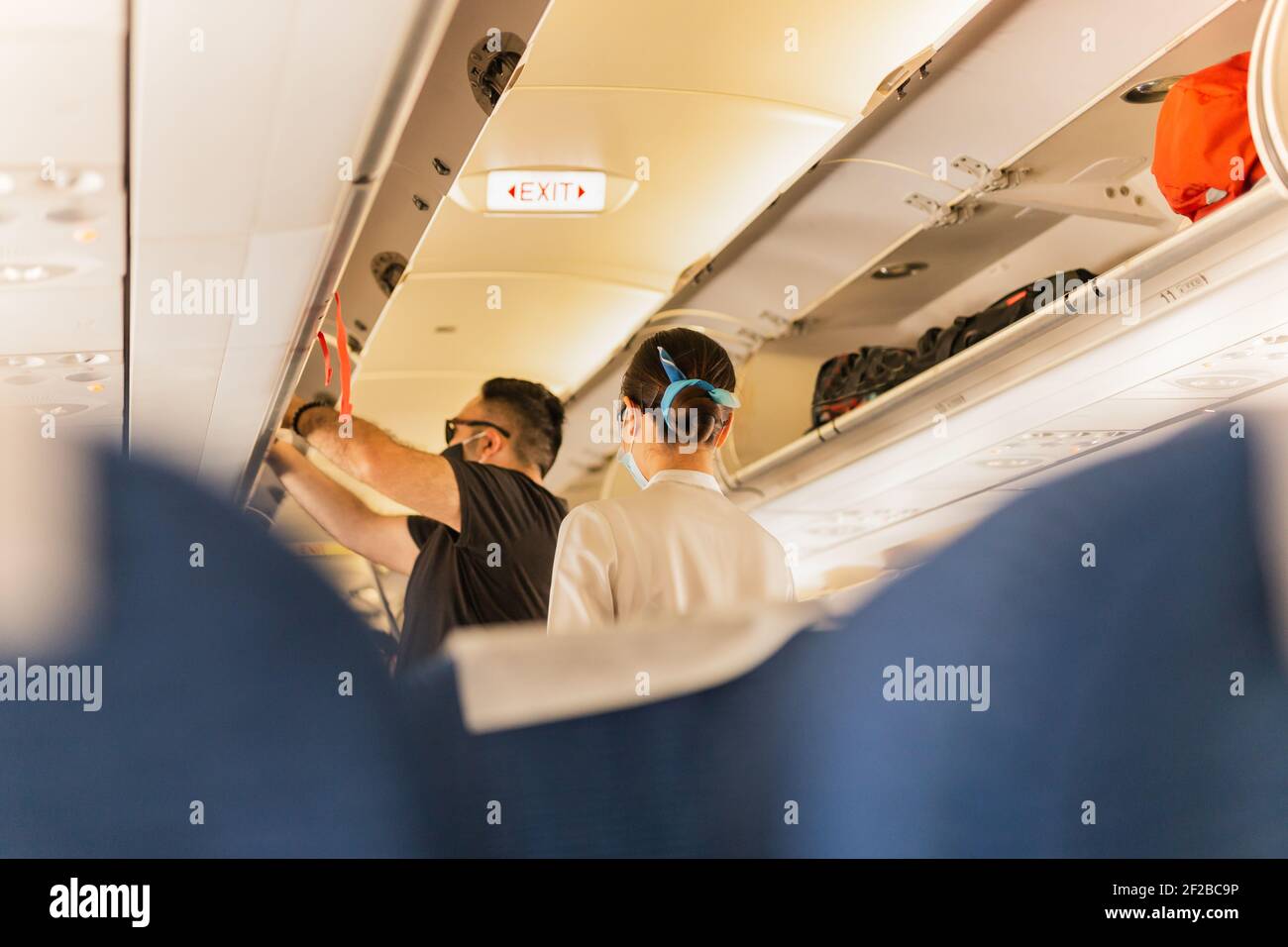Flight atttendant attendant helping passenger to put luggage cabin compartment. Stock Photo